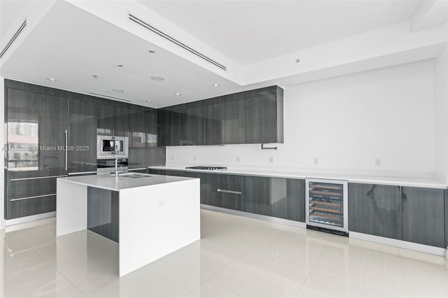 kitchen featuring beverage cooler, an island with sink, stainless steel gas stovetop, a sink, and modern cabinets
