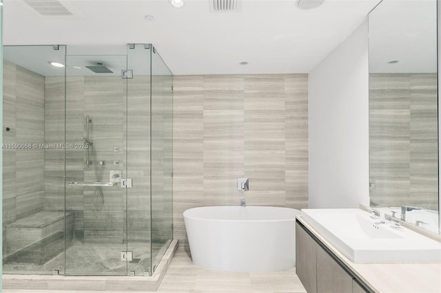 bathroom with tile walls, vanity, a stall shower, a freestanding bath, and visible vents