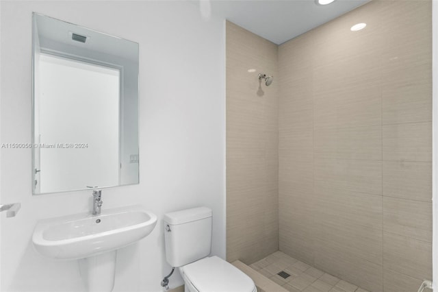 bathroom featuring tiled shower, sink, and toilet