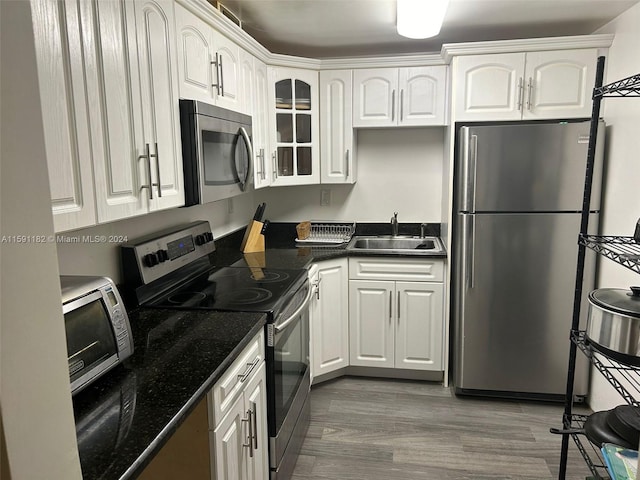 kitchen with stainless steel appliances, hardwood / wood-style flooring, white cabinetry, dark stone countertops, and sink