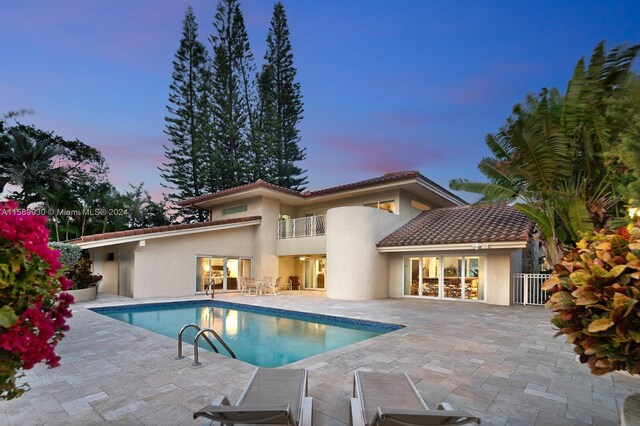 pool at dusk featuring a patio and a hot tub