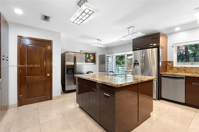 kitchen with hanging light fixtures, light tile patterned floors, an island with sink, stainless steel appliances, and light stone countertops