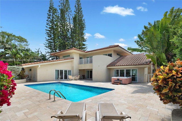 back of house featuring a balcony, a pool with hot tub, and a patio area