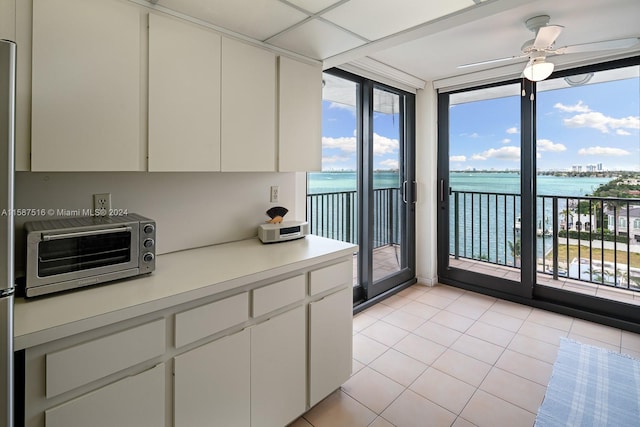 kitchen with light tile patterned floors, a wall of windows, a water view, and white cabinets