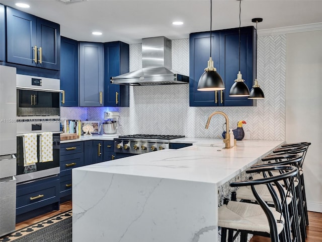 kitchen with appliances with stainless steel finishes, wall chimney exhaust hood, light stone countertops, and hanging light fixtures