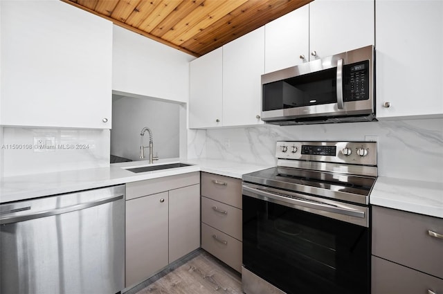 kitchen with stainless steel appliances, light wood-type flooring, wood ceiling, backsplash, and sink