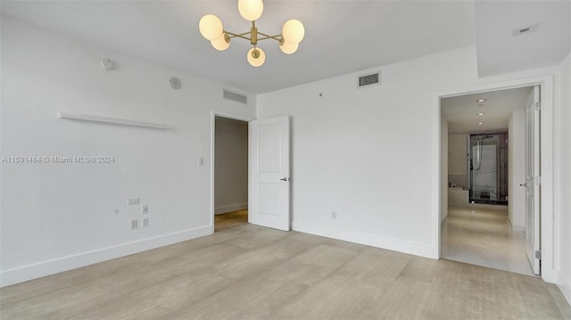 empty room featuring a notable chandelier and light wood-type flooring