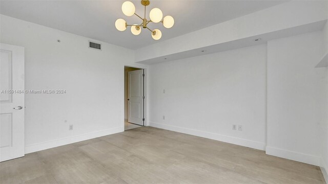 unfurnished room featuring a chandelier and light hardwood / wood-style flooring