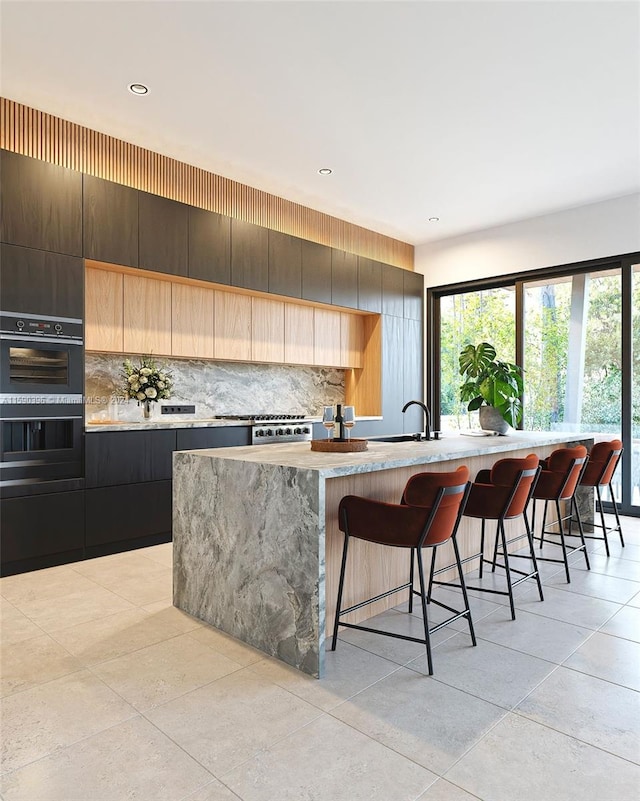 kitchen with light tile floors, tasteful backsplash, a breakfast bar, and a kitchen island with sink