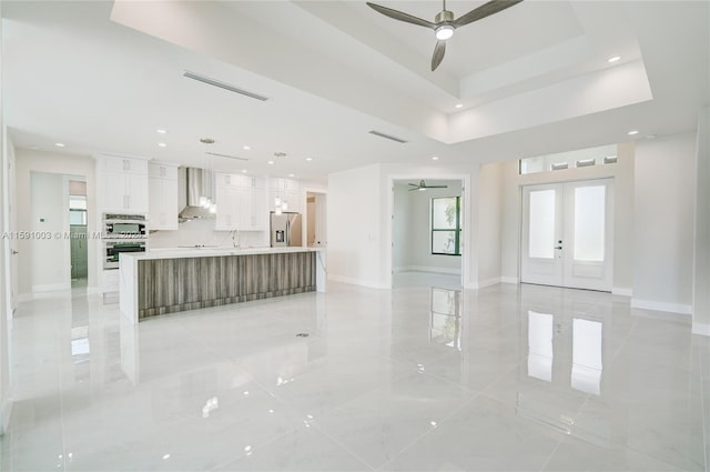 unfurnished living room featuring french doors, light tile patterned floors, a tray ceiling, and ceiling fan