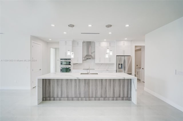 kitchen with a center island with sink, pendant lighting, stainless steel appliances, light tile patterned floors, and wall chimney range hood