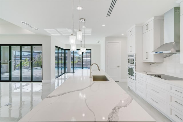 kitchen with pendant lighting, black electric stovetop, sink, light stone counters, and wall chimney exhaust hood