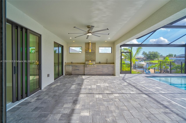 view of patio featuring ceiling fan, sink, glass enclosure, and an outdoor kitchen