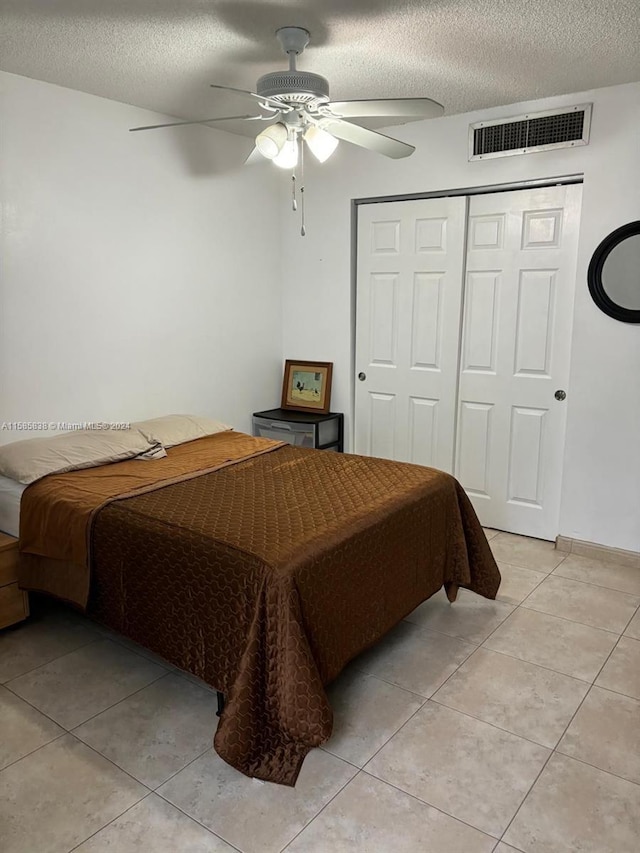 bedroom featuring ceiling fan, light tile patterned floors, a textured ceiling, and a closet