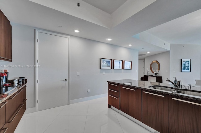 kitchen with dark brown cabinets, light tile patterned flooring, sink, and dark stone counters