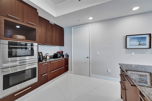 kitchen featuring cooktop, dark stone countertops, light tile patterned floors, and double oven