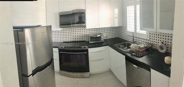 kitchen featuring appliances with stainless steel finishes, white cabinets, backsplash, sink, and light tile floors