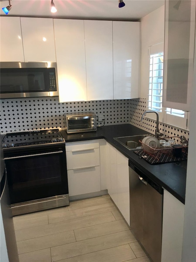 kitchen featuring stainless steel appliances, tasteful backsplash, white cabinetry, light wood-type flooring, and sink