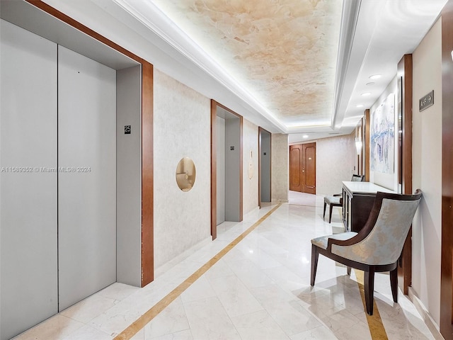 hallway with a raised ceiling, light tile flooring, and elevator