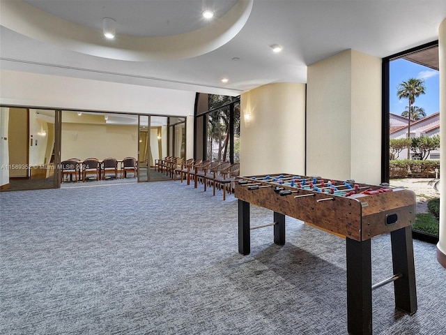 playroom featuring a raised ceiling, dark colored carpet, and a wall of windows