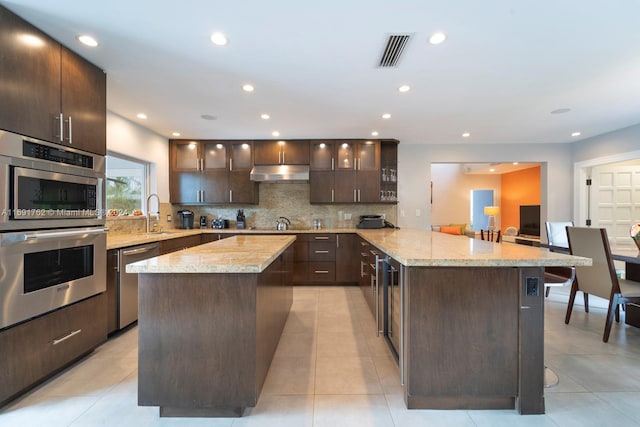 kitchen featuring dark brown cabinetry, tasteful backsplash, kitchen peninsula, a breakfast bar area, and appliances with stainless steel finishes