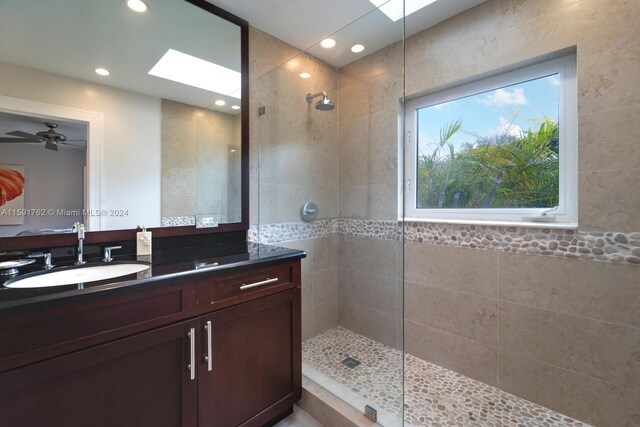 bathroom featuring a tile shower, vanity, a skylight, and ceiling fan