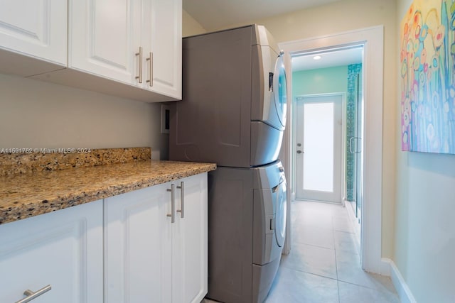 laundry room with cabinets, stacked washer / dryer, and light tile patterned flooring