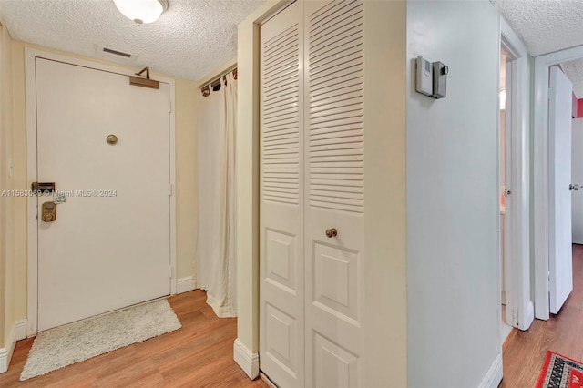 hallway with light wood-type flooring, visible vents, a textured ceiling, and baseboards