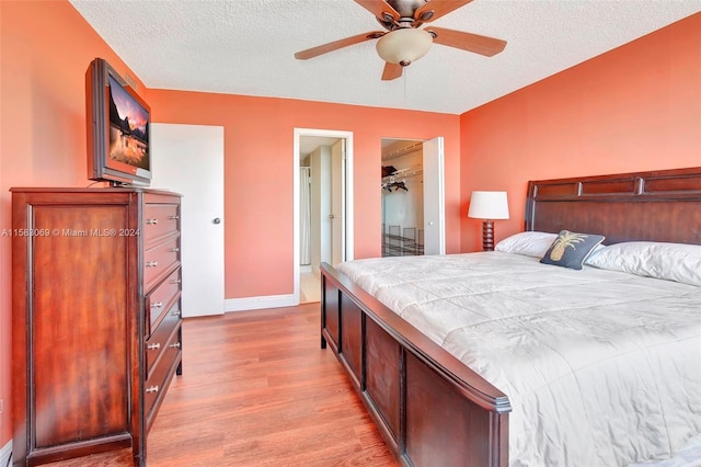 bedroom with a closet, ceiling fan, a walk in closet, wood-type flooring, and a textured ceiling