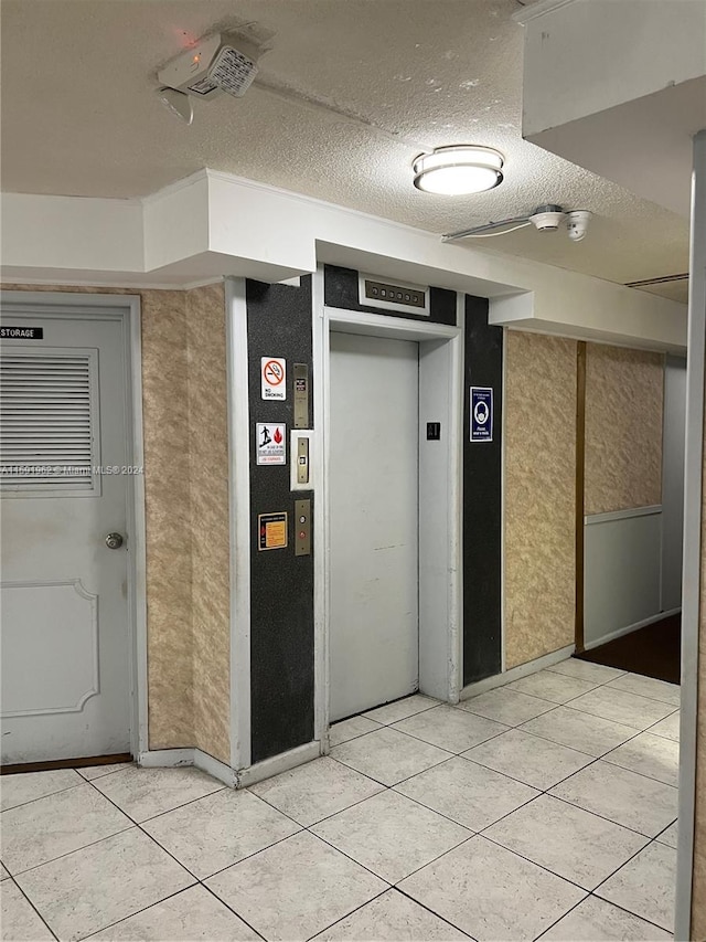 corridor featuring a textured ceiling, elevator, and light tile floors