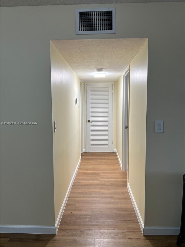 corridor with light hardwood / wood-style floors and a textured ceiling