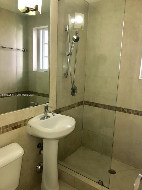 bathroom with a shower with door, tile walls, and toilet