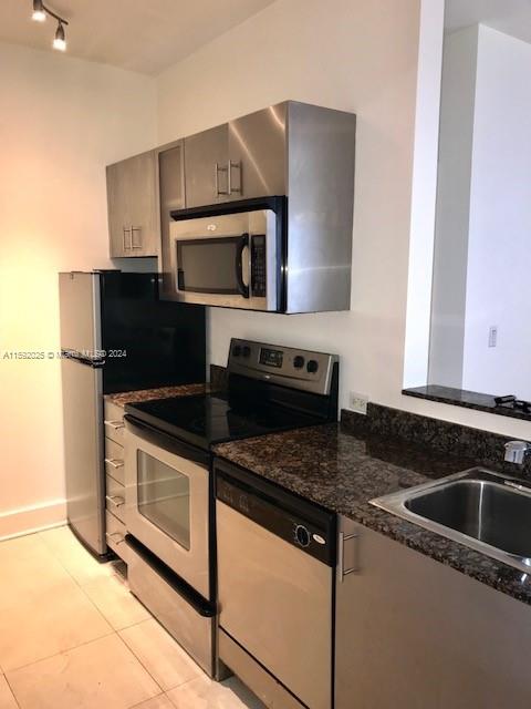 kitchen with sink, light tile patterned floors, dark stone counters, and appliances with stainless steel finishes