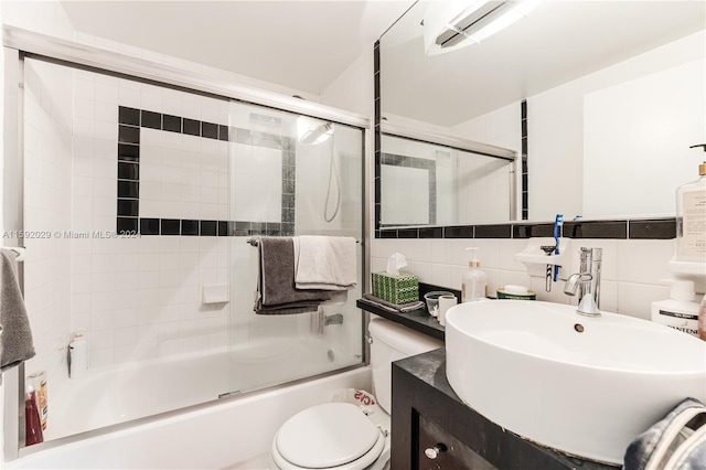 full bathroom featuring oversized vanity, tasteful backsplash, bath / shower combo with glass door, tile walls, and toilet