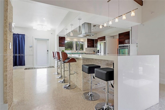 kitchen featuring tasteful backsplash, a kitchen breakfast bar, island exhaust hood, kitchen peninsula, and stainless steel appliances