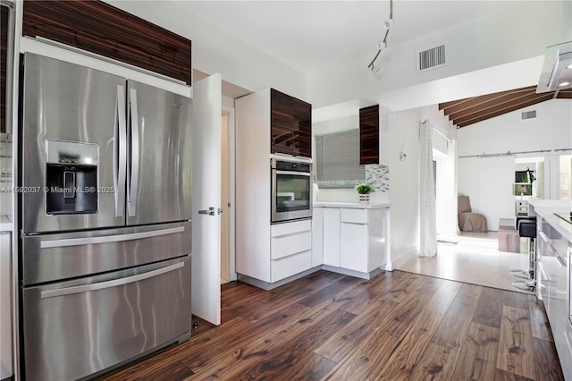 kitchen featuring dark wood-type flooring, appliances with stainless steel finishes, dark brown cabinetry, decorative backsplash, and vaulted ceiling