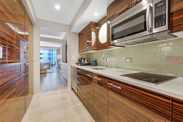 kitchen featuring backsplash, sink, black electric cooktop, and light tile flooring