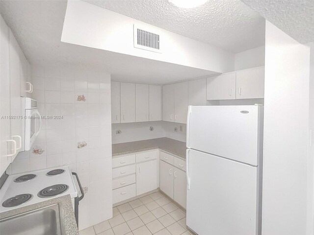 kitchen with sink, a textured ceiling, light tile patterned floors, and white appliances