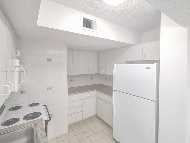 kitchen featuring a textured ceiling, white cabinets, white appliances, and light tile patterned floors