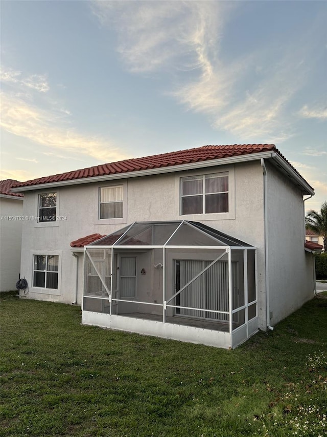 back house at dusk featuring a sunroom and a yard