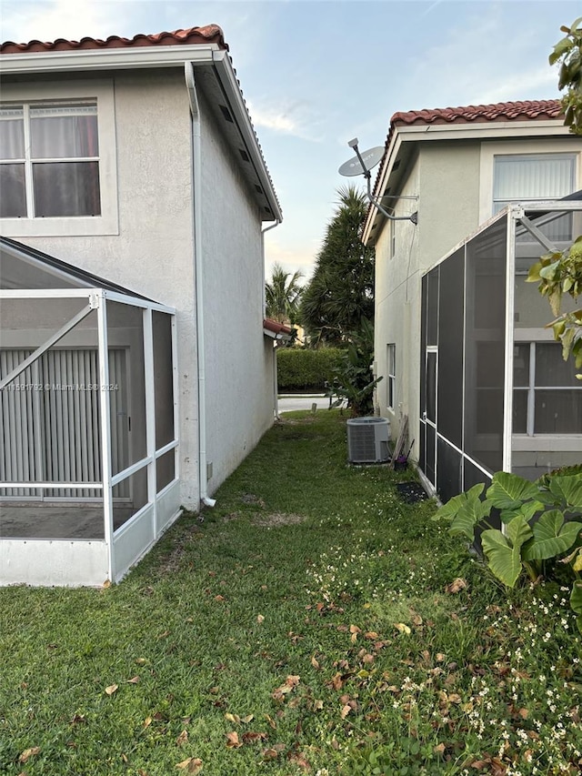 view of side of home with central AC, a sunroom, and a yard