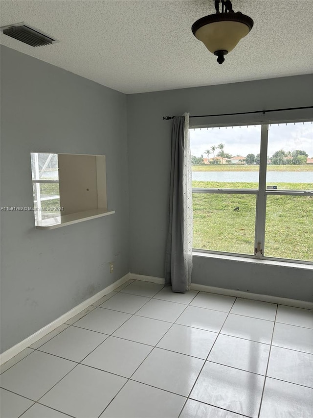 spare room featuring a water view, light tile flooring, and a textured ceiling