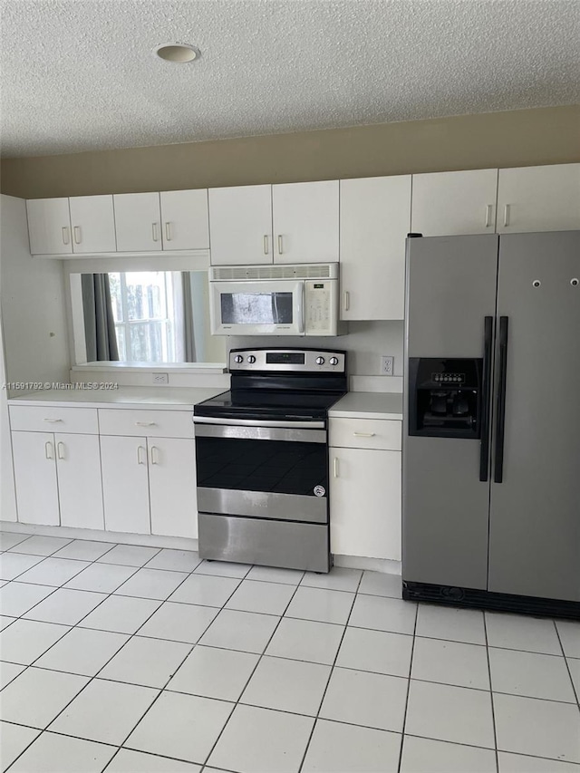 kitchen with a textured ceiling, light tile floors, white cabinetry, and appliances with stainless steel finishes