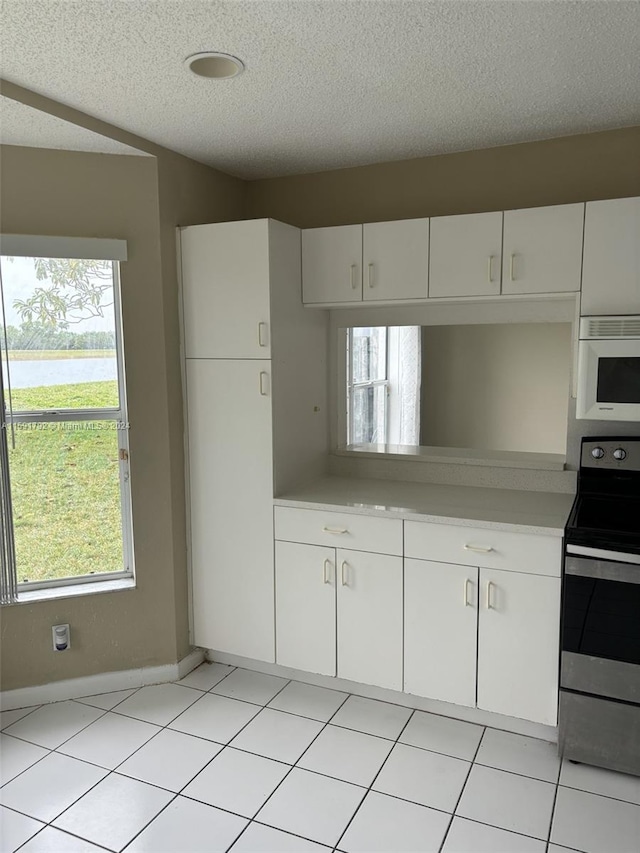 kitchen featuring a textured ceiling, electric range, white cabinets, and light tile flooring