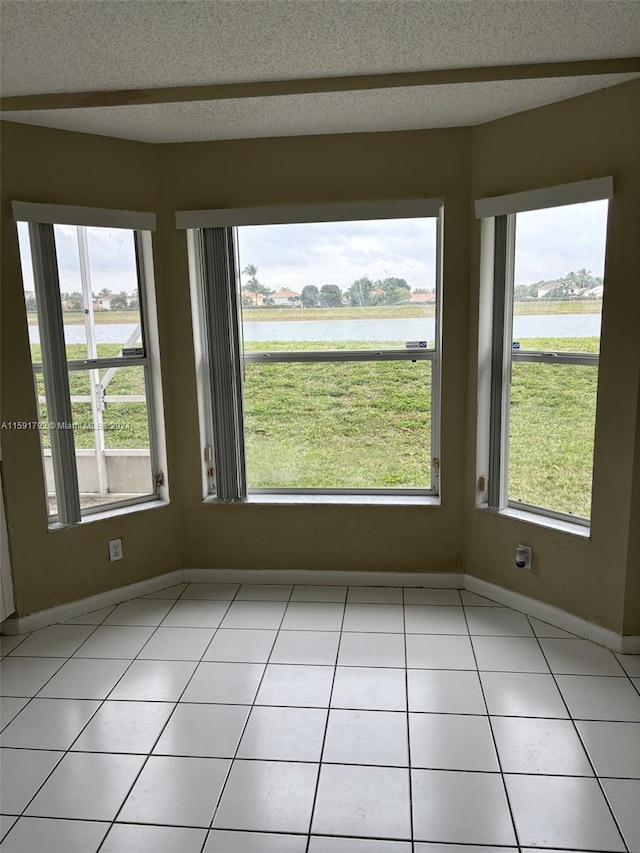 unfurnished room with a textured ceiling, a water view, and light tile floors