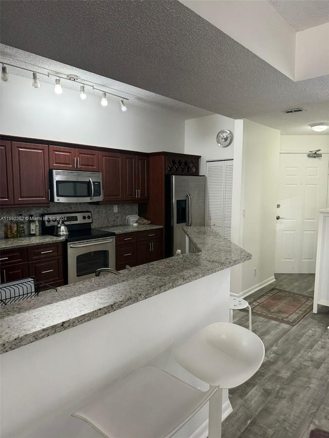 kitchen featuring dark hardwood / wood-style floors, tasteful backsplash, track lighting, a kitchen bar, and appliances with stainless steel finishes