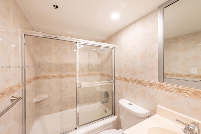 full bathroom featuring sink, tile walls, toilet, and bath / shower combo with glass door