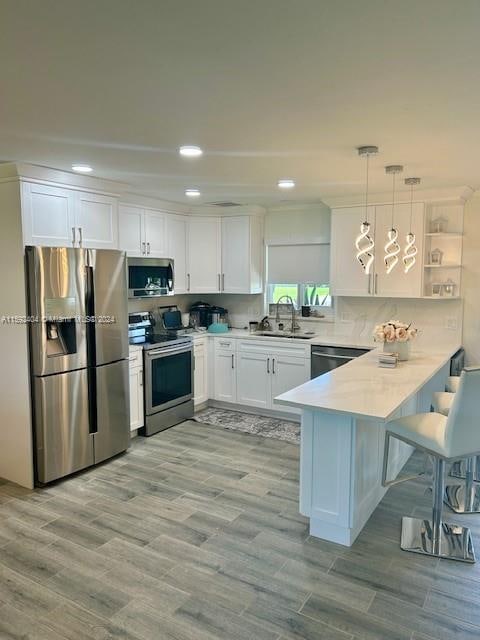 kitchen featuring white cabinetry, light hardwood / wood-style flooring, appliances with stainless steel finishes, kitchen peninsula, and sink