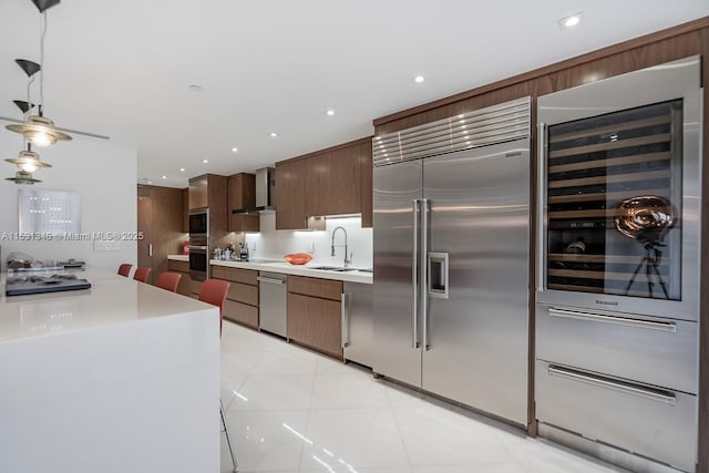 kitchen featuring built in appliances, wine cooler, light countertops, wall chimney range hood, and pendant lighting