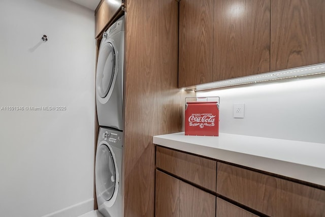 laundry area featuring stacked washer / drying machine and cabinet space